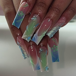 May include: Long, square acrylic nails with a pink, green, and blue gradient design. Some nails feature floral accents and rhinestones. The nails have a glossy finish and a 3D effect.