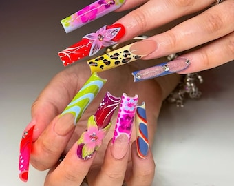 May include: A hand displaying long, colorful acrylic nails. Designs include floral patterns, animal prints, and abstract shapes in shades of pink, red, yellow, blue, and green. Some nails feature 3D flower embellishments and rhinestones.