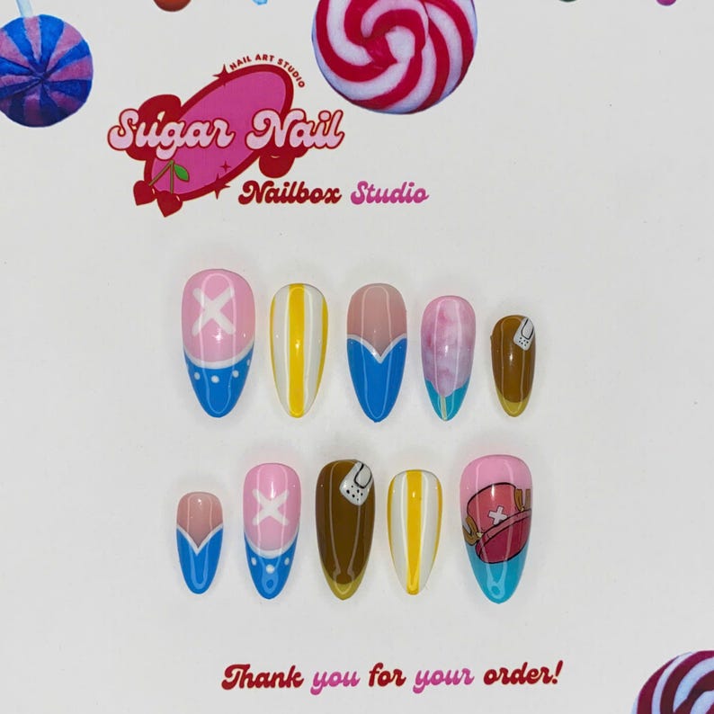 May include: A collection of custom press-on nails with diverse designs. The nails showcase a blend of pink, blue, yellow, and brown, with cartoon artwork and the text "Sugar Nail Nailbox Studio" and "Thank you for your order!"