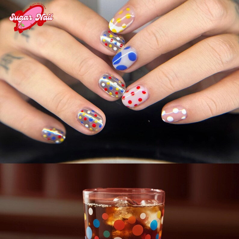 K&ouml;nnte beinhalten: Nahaufnahme einer Hand mit einer Manik&uuml;re mit bunten Tupfen auf transparenten N&auml;geln. Die N&auml;gel haben verschiedene Farben, darunter Rot, Gelb, Blau und Wei&szlig;. Das Bild zeigt auch ein Glas dunkles Getr&auml;nk mit Eis und Tupfen.