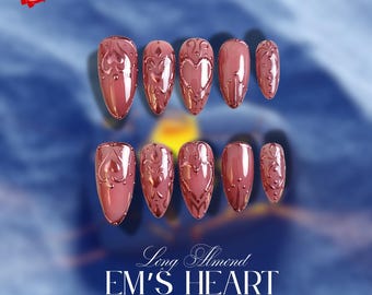 Può includere: Un set di dieci unghie finte lunghe a forma di mandorla, di colore rosa antico. Ogni unghia presenta un design in rilievo ornato con cuori e volute. Il testo "EM'S HEART" è visualizzato sotto.