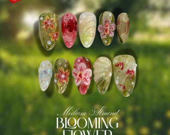 May include: A set of ten almond-shaped artificial nails with floral designs. The nails feature a variety of colors, including green, red, and white, with intricate details. The text "Medium Almond BLOOMING FLOWER" is displayed.