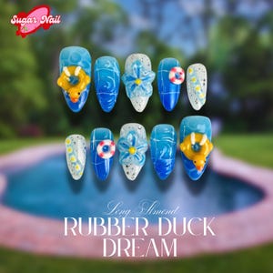 Puede incluir: Un conjunto de uñas artificiales largas en forma de almendra con temática veraniega. Las uñas presentan diseños azules y blancos, incluyendo un patito de goma, un salvavidas y detalles florales. Se muestra el texto "RUBBER DUCK DREAM".