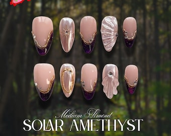 May include: A set of almond-shaped press-on nails in a Solar Amethyst design. The nails feature a nude base with gold accents, purple glitter tips, and various embellishments, including rhinestones and a shell-like design. The text "Sugar Nail" is in the top left corner.