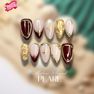 May include: A set of medium almond-shaped pearl nails. The nails feature burgundy, gold starbursts, and gold textured accents. The text "Medium Almond PEARL" is at the bottom. The nails are approximately 2 cm in length.