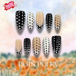 May include: A set of long almond-shaped press-on nails with a polka dot design. The nails feature a variety of colors, including black, white, and beige, with the text "DOTS POLKA". The Sugar Nail logo is in the upper left corner.