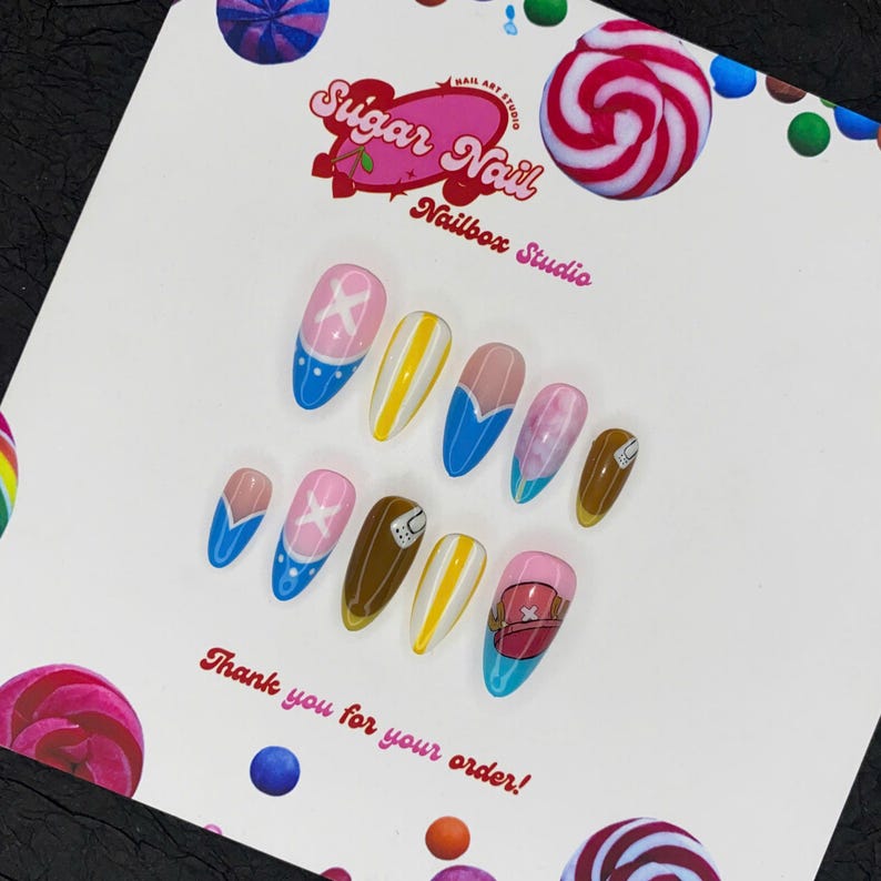 May include: A collection of custom nail art designs in a variety of colours and patterns. The designs include blue, pink, yellow, and brown nails with cartoon character art. The Sugar Nail Nailbox Studio logo and the text "Thank you for your order!" are visible.