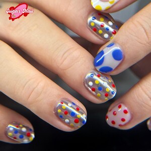 K&ouml;nnte beinhalten: Nahaufnahme von manik&uuml;rten N&auml;geln mit klarem Nagellack und bunten Tupfen. Die Punkte sind rot, gelb, blau und wei&szlig;. Die N&auml;gel sind sauber geformt und das Design ist einheitlich. Das Bild enth&auml;lt den Text "Sugar Nail".