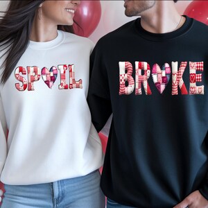 Könnte beinhalten: Ein Paar trägt passende Sweatshirts. Eines ist weiß mit dem Wort "SPOIL" in einem Patchwork-Design mit einem Herz. Das andere ist schwarz mit dem Wort "BROKE" in einem ähnlichen Patchwork-Design mit einem Herz. Ballons sind im Hintergrund.