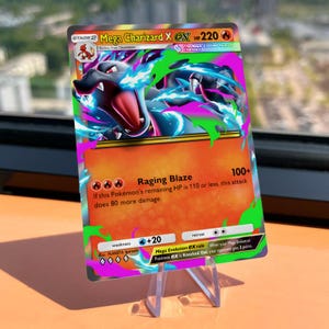 Op de afbeelding: Een Mega Charizard X EX ruilkaart met een zwarte draak met blauwe vlammen tegen een levendige oranje achtergrond. De kaart bevat de tekst Raging Blaze, 220 HP en gedetailleerde spelregels en aanvalsstatistieken in het Engels.