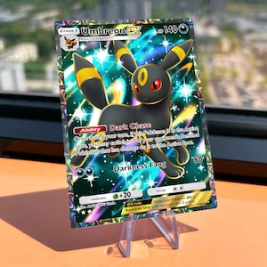 Op de afbeelding: Een holografische Umbreon EX ruilkaart met een zwart wezen met gele ringen, rode ogen en de Dark Chase-vaardigheid. De kaart toont 140 HP, de Darkness Fang-aanval en tekst met spelregels tegen een achtergrond vol sterren.