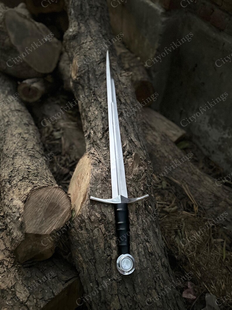 May include: A silver sword with a black handle and a crossguard. The sword is displayed against a backdrop of stacked logs. The text "Cityofvikings" is visible in the background.