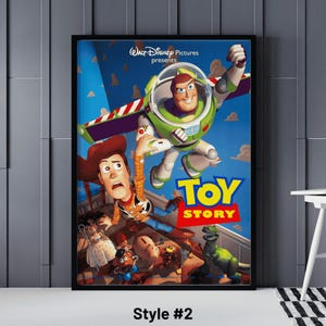 May include: A framed poster featuring the Toy Story movie. The poster shows Buzz Lightyear in a green and white spacesuit, Woody in a cowboy hat, and other characters. The title "Toy Story" is in large, colorful letters.