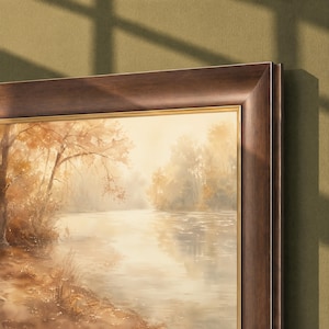 May include: A framed landscape painting depicting a calm river scene during autumn. The artwork features soft golden and brown tones, with trees lining the riverbank under a hazy sky. The painting is enclosed in a dark brown wooden frame.
