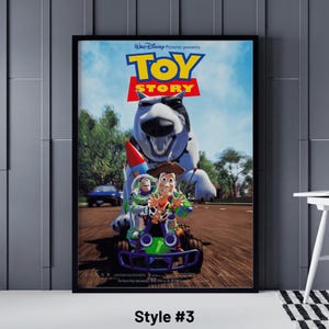 May include: Framed poster featuring the Toy Story movie. The poster shows the characters Woody, Buzz Lightyear, and others in a race scene. The title "Toy Story" is prominently displayed in large, colorful letters. The poster is framed in black.