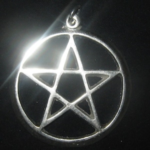 May include: A silver pendant in the shape of a pentagram, a five-pointed star, with a circular frame. The pendant is on a black background.