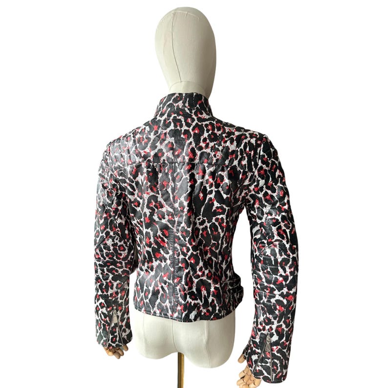 May include: A black, red, and white leopard print jacket with a stand-up collar and long sleeves. The jacket is displayed on a mannequin and features a zipper detail on the sleeves.