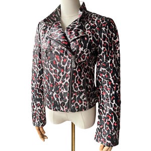 May include: A black, red, and white leopard print jacket with a zipper closure and a notched collar. The jacket has long sleeves and a fitted silhouette. The jacket is displayed on a mannequin.