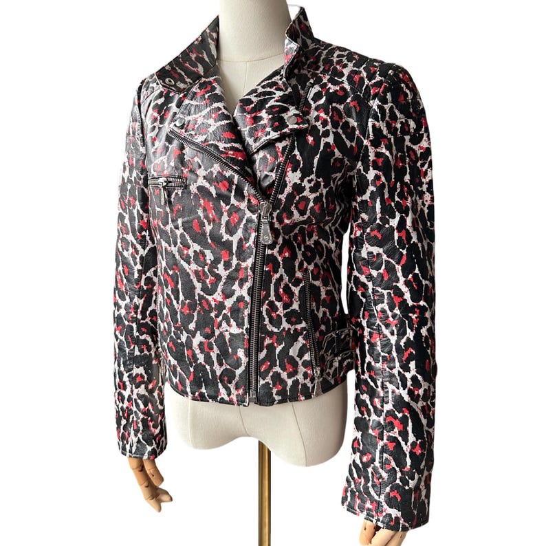 May include: A black, red, and white leopard print jacket with a zipper closure and a notched collar. The jacket has long sleeves and a fitted silhouette. The jacket is displayed on a mannequin.