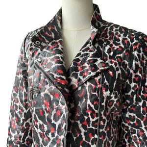 May include: A black, red, and white leopard print jacket with a classic biker style. The jacket features a notched collar, a diagonal zipper closure, and a small zippered pocket. The jacket is displayed on a mannequin.