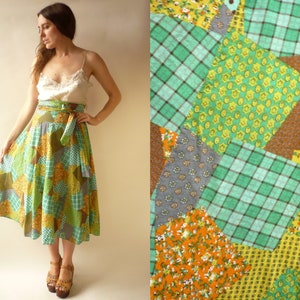 May include: A patchwork skirt in shades of green, yellow, and brown. The skirt has a wrap design with a matching tie. The fabric is patterned with various geometric and floral designs. The skirt is paired with a cream-coloured camisole.