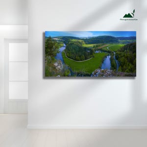 May include: A scenic photograph of a river meandering through a valley, featuring vibrant green fields and thick forests. The image is set against a blue sky, with the text "Photogaleriejoachim" visible in the top right corner.