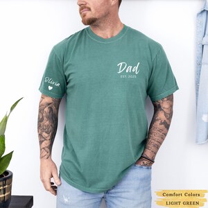 Może przedstawiać: Jasnozielony t-shirt z napisem "Dad Est. 2025" z przodu i napisem "Olivia" z sercem na lewym rękawie.