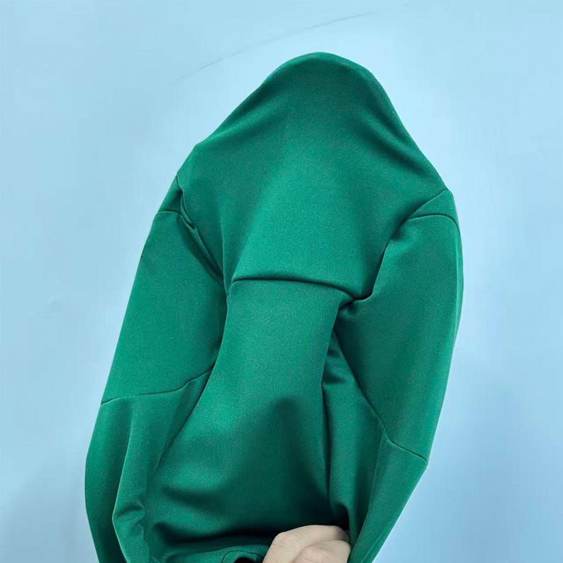 Puede incluir: Una sudadera con capucha verde hecha de una tela lisa y brillante. La sudadera tiene un dise&ntilde;o sencillo con capucha y mangas largas. El fondo es de color azul claro.
