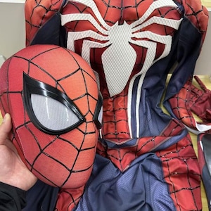 Könnte beinhalten: Ein rot-blaues Spider-Man-Kostüm mit einem weißen Spinnenlogo auf der Brust. Das Kostüm beinhaltet eine separate rot-schwarze Maske mit einem weißen Netz-Augenstück.