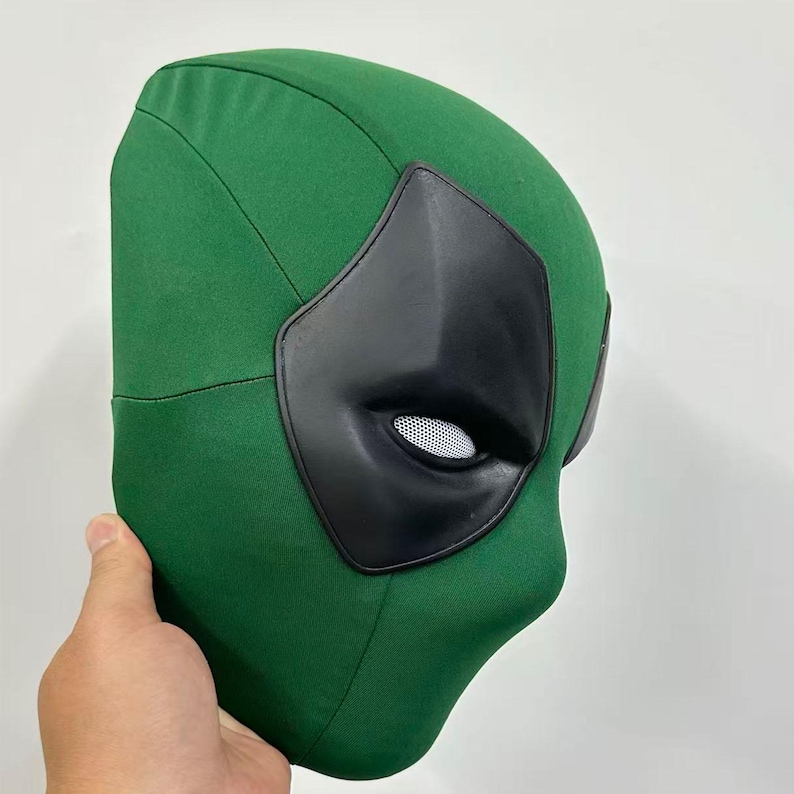 Puede incluir: Una m&aacute;scara de tela verde con cubiertas oculares negras y un &aacute;rea ocular de malla blanca. La m&aacute;scara est&aacute; dise&ntilde;ada para cubrir toda la cara. La m&aacute;scara est&aacute; sujeta por una mano.