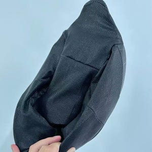Puede incluir: Un sombrero de pescador negro con un patr&oacute;n texturizado en forma de rejilla. El sombrero est&aacute; hecho de un material flexible y tiene una corona redondeada y un ala ligeramente curvada. El sombrero se muestra sobre un fondo azul claro.
