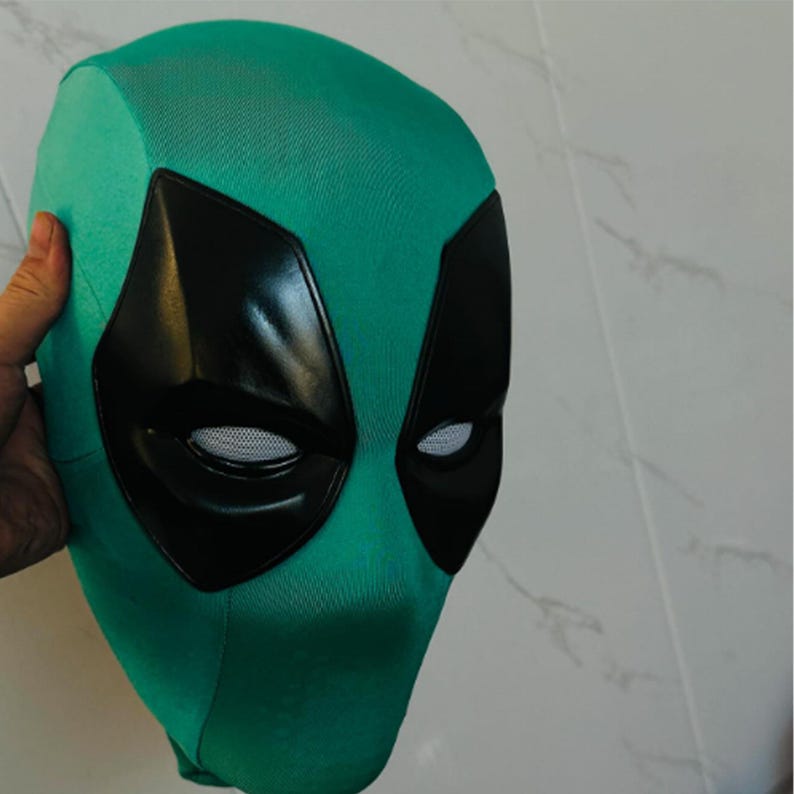 Puede incluir: Una m&aacute;scara de color verde azulado con cubiertas oculares negras y aberturas oculares de malla blanca. La m&aacute;scara est&aacute; sujeta por una mano y es probablemente un accesorio de disfraz. La m&aacute;scara est&aacute; dise&ntilde;ada para cubrir toda la cabeza.