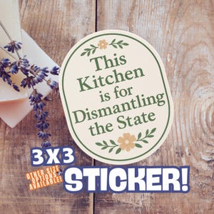 May include: Oval sticker with the text "This Kitchen is for Dismantling the State" in green and cream colors. The sticker is 3x3 inches and has floral accents. The word "STICKER!" is in a blue banner.