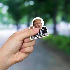 May include: A sticker featuring a photo of Donald Trump speaking into a microphone with the text "Just like my hands, Just like my legacy".