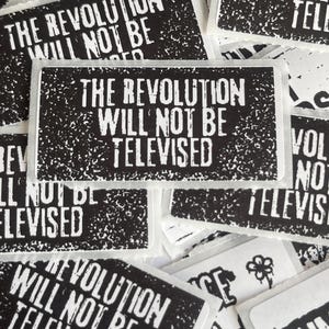 May include: A collection of black and white stickers with the phrase "THE REVOLUTION WILL NOT BE TELEVISED" in bold, distressed font. The stickers have a rectangular shape with rounded corners and a textured background.