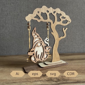 Pode incluir: Decoração em madeira de um gnomo num baloiço, segurando uma chávena de café, debaixo de uma árvore. O gnomo é de cor clara, com um chapéu pontudo e barba. A árvore tem um design recortado detalhado. A base inclui o texto "Ai, eps, svg, CDR".