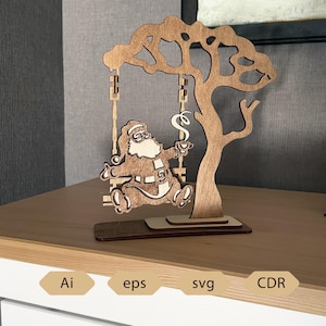 May include: A wooden Christmas ornament depicting Santa Claus on a swing, made from light brown wood. The swing hangs from a tree-shaped structure. Santa is holding a cup, and the design is laser cut.