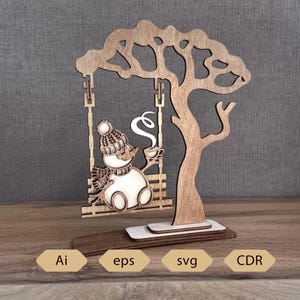 Op de afbeelding: Houten decoratie van een sneeuwpop op een schommel, met een kopje koffie, met een boomvormige achtergrond. De sneeuwpop draagt een muts en sjaal. Ai, eps, svg en CDR.