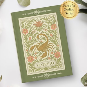 以下が含まれることがあります： 緑色の本。花柄のデザインと金のサソリのイラスト。表紙には「SCORPIO」の文字。この本は、星座シリーズの一部です。綿と葉が本を囲んでいます。