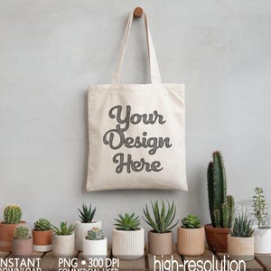 May include: A cream-colored tote bag with the text "Your Design Here" in a glittery font hangs from a wooden peg. Various potted succulents and cacti are arranged below on a wooden surface. The image also includes text that says "INSTANT DOWNLOAD PNG 300 DPI COMMERCIAL USER high-resolution".