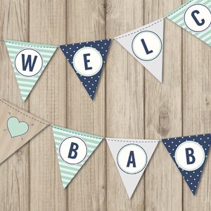 May include: A blue and green welcome baby banner with white letters in circles. The banner is made of felt and has a rustic wood background.