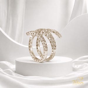 May include: Two silver-toned eternity rings featuring a continuous band of small, clear, round-cut stones set in metal. The rings are positioned upright, one slightly behind the other, showcasing a uniform, sparkling design throughout the entire circumference.