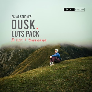 Puede incluir: Imagen de una persona sentada en una ladera cubierta de hierba con un fondo montañoso. La imagen presenta el texto "ECLAT STUDIO'S DUSK. LUTS PACK 10 LUTS + POWERGRADE" en blanco y rojo. El logotipo de ECLAT STUDIO está en la esquina superior derecha.