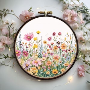 May include: An embroidered floral design in a wooden hoop. The artwork depicts a colourful meadow with pink, yellow, orange, and purple wildflowers. The embroidery is set in a dark wooden hoop, with a gold-toned clasp.