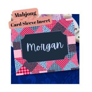 May include: A rectangular Mahjong card sleeve insert featuring a patchwork pattern of pink, red, and dark blue geometric shapes with stars, stripes, and dots. A central dark blue label with a scalloped border displays the name Morgan in white.