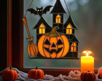 May include: A Halloween-themed stained glass window decoration featuring a black haunted house, a jack-o'-lantern, and a bat. An orange broom hangs to the left. The window is hanging in front of a window sill with pumpkins and a lit candle.