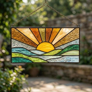 Könnte beinhalten: Buntglasfenster mit einem Sonnenuntergang über sanften Hügeln. Die Sonne ist leuchtend gelb, mit orangefarbenen und goldenen Strahlen. Die Hügel sind grün und blau, mit einer Kette zum Aufhängen.