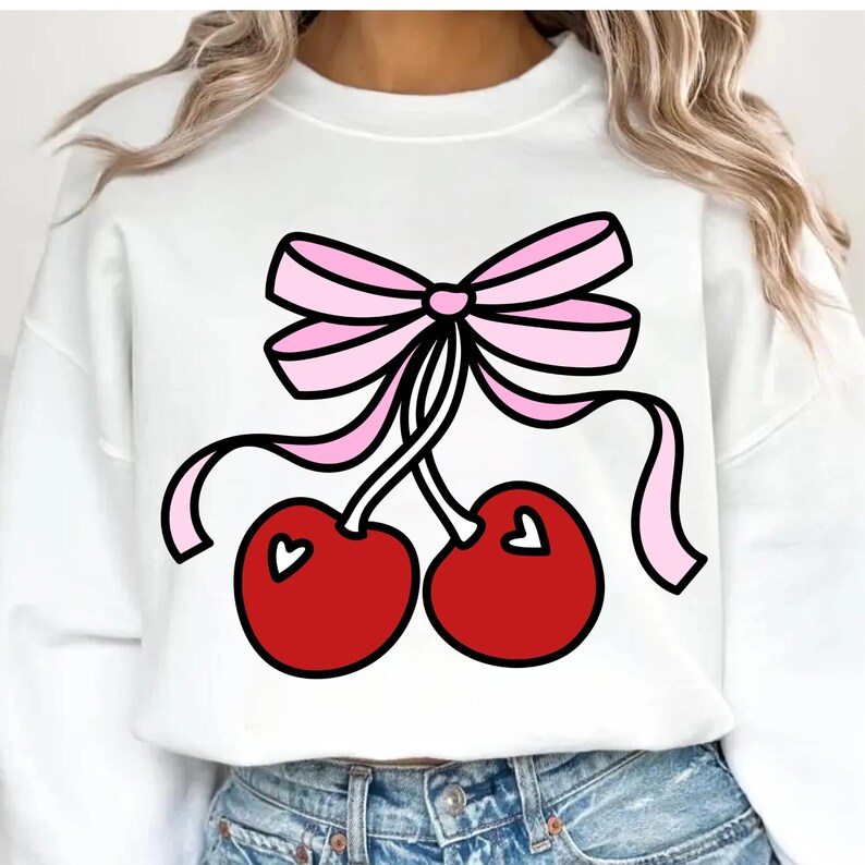 May include: White sweatshirt featuring a graphic of two red cherries with heart-shaped details, tied with a pink bow. The design is outlined in black. The sweatshirt is a casual, everyday garment.