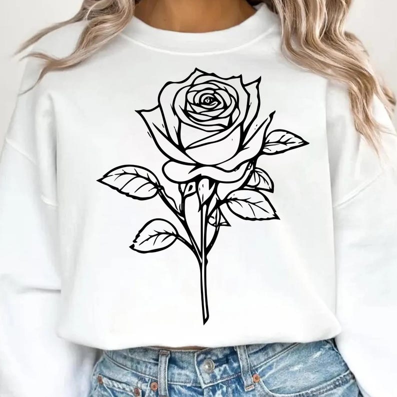 May include: White sweatshirt featuring a large black and white rose graphic. The rose is detailed with petals and leaves, creating a botanical design. The sweatshirt is a casual style, suitable for everyday wear.