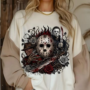 May include: A cream-colored sweatshirt featuring a graphic print of three horror movie characters: a hockey mask, a man in a fedora with clawed gloves, and a man holding a knife. The design includes red roses, thorny vines, and flames.
